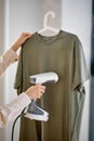 Female steams clothes on hanger. Woman with steamer cleaning clothes side view