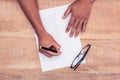 Cropped hand of businessman writing on paper by eye glasses at desk