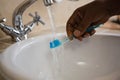 Cropped hand on man washing toothbrush in bathroom sink