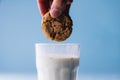 Cropped hand of person dipping cookie in milk against blue background, copy space