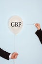Cropped hands holding needle and popping balloon with text saying GBP