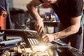 Cropped hands of unrecognizable mechanic. Close up. Repairman with screwdriver and shining lamp working under car hood