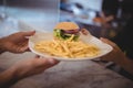 Cropped hands of waiter and female chef holding fresh burger and fries plate at counter Royalty Free Stock Photo