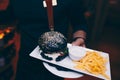 Cropped hands of waiter Japanese Black Burger with Cheese. Cheeseburger with potatoes in the hands holding plateau dish holding pl Royalty Free Stock Photo