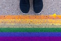 Cropped humans legs in black shoes standing on asphalt in front of lgbt rainbow colored flag, gender identity and self-