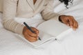 Cropped image of African-American woman lying in bed and making notes in diary. Royalty Free Stock Photo