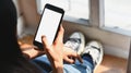 Cropped image of artist woman legs with jeans sitting on wooden floor while holding white blank screen smartphone in hands. Royalty Free Stock Photo