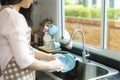 Cropped image of Asian attractive young woman is washing dishes in sink in kitchen while doing cleaning at home