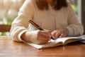 Cropped image of an Asian woman in casual clothes writing something in her book at a table indoors Royalty Free Stock Photo