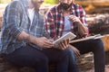 cropped image of bearded lumberjacks sitting on logs with axe and digital tablet