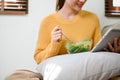 Beautiful Asian woman eating salad vegetables mix while watching something on tablet Royalty Free Stock Photo