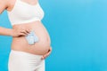 Cropped image of blue socks for a baby boy in pregnant woman`s hand against her belly at blue background. Waiting for a future