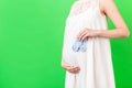 Cropped image of blue socks for a baby boy in pregnant woman`s hand against her belly at green background. Waiting for a future