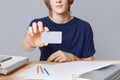 Cropped image of casually dressed young male enterpreneur holds card with blnk copy space, sits on working table, sorrounded with Royalty Free Stock Photo