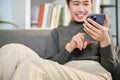 Cropped image, Charming Asian woman using her phone while relaxing on sofa in living room