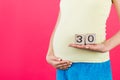 Cropped image of cubes with thirty weeks of pregnancy in pregnant woman`s hands wearing colorful home clothing at pink background