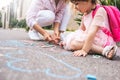 Cropped image of cute little girl and mother drawing with colorful chalks on the sidewalk. Caucasian blonde female play together Royalty Free Stock Photo