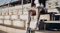 Cropped image of disabled african american sportswoman with prosthesis legs in sportswear sitting on stairs at stadium. Generative