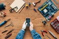 cropped image of electronic engineer with prosthetic arm using smartphone at table surrounded