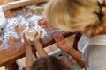 Cropped image of a female and kid hands holding dough in heart shape top view. Baking ingredients on the wooden table. Royalty Free Stock Photo