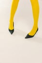 Cropped image of female legs in yellow bright tights and heels isolated over grey studio background. Colorful outfit Royalty Free Stock Photo