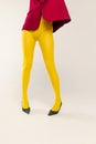 Cropped image of female legs in yellow bright tights and heels isolated over grey studio background. Weird style Royalty Free Stock Photo