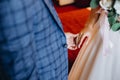 Cropped image of groom in blue suit holding bride`s hand against red wall background indoors. Wedding details.