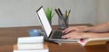 Cropped image of hands is typing on a white blank screen computer laptop that putting on a wooden working desk. Royalty Free Stock Photo