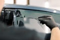 Cropped image of hands of worker in garage tinting a car window with tinted foil or film, holding special blade or knife Royalty Free Stock Photo