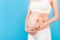 Cropped image of happy pregnant woman in white underwear holding teddy bear against her belly at blue background. Child expecting Royalty Free Stock Photo