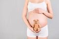 Cropped image of happy pregnant woman in white underwear holding teddy bear against her belly at gray background. Child expecting Royalty Free Stock Photo