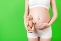 Cropped image of happy pregnant woman in white underwear holding teddy bear against her belly at green background. Child expecting Royalty Free Stock Photo