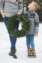 Cropped image of legs of mother and son, holding together beautiful Christmas wreath, standing outdoors in winter park Royalty Free Stock Photo