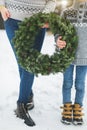 Cropped image of legs of mother and son, holding together beautiful Christmas wreath, standing outdoors in winter park