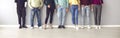 Cropped image of the legs of people in ordinary clothes and shoes standing in a row near the wall.