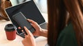 Cropped image of long hair woman holding smartphone in her hands in front a computer tablet next to takeaway coffee cup. Royalty Free Stock Photo