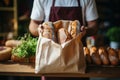 Cropped image of male bakery owner or employee holding freshly baked wheat bread loaves packed in craft paper bag. High Royalty Free Stock Photo
