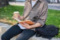 A cropped image of a male college student sits on a stone bench in a park, reading a book outdoors