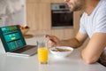 cropped image of man eating flakes with milk at kitchen table with fresh juice in glass and laptop with sportsbet