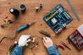 cropped image of man with prosthetic arm holding wires and screwdriver surrounded by instruments