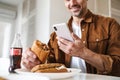 Cropped image of man smiling and using smartphone while have lunch