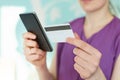 Cropped image of modern smart phone and plastic card in woman`s hands against blue blurred background. Young businesswoman checks Royalty Free Stock Photo