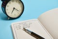 Cropped image of an open organizer with plans for the day, ink pen and alarm clock on blue background with copy space Royalty Free Stock Photo