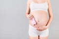 Cropped image of pink socks for a baby girl in pregnant woman`s hands against her belly at gray background. Parenthood concept. Royalty Free Stock Photo