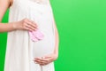 Cropped image of pink socks for a baby girl in pregnant woman`s hands against her belly at green background. Parenthood concept. Royalty Free Stock Photo