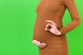 Cropped image of positive pregnant woman in brown dress showing okay gesture against her belly at green background. Easy and happy Royalty Free Stock Photo