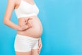 Cropped image of positive pregnant woman in white underwear showing okay gesture against her belly at blue background. Easy and Royalty Free Stock Photo