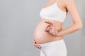 Cropped image of positive pregnant woman in white underwear showing okay gesture against her belly at gray background. Easy and Royalty Free Stock Photo