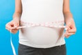 Cropped image of pregnant woman in home clothing measuring her growing abdomen at blue background. Inch tape measure. Copy space Royalty Free Stock Photo