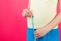 Cropped image of pregnant woman in home clothing measuring her growing abdomen at pink background. Inch tape measure. Copy space Royalty Free Stock Photo